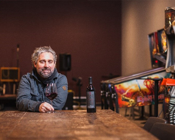 chris gorman smiling drinking wine at bar with pin ball machines